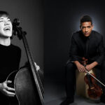 Josh and Julia Henderson, Julia with a cello laughing and Josh holding his violin.