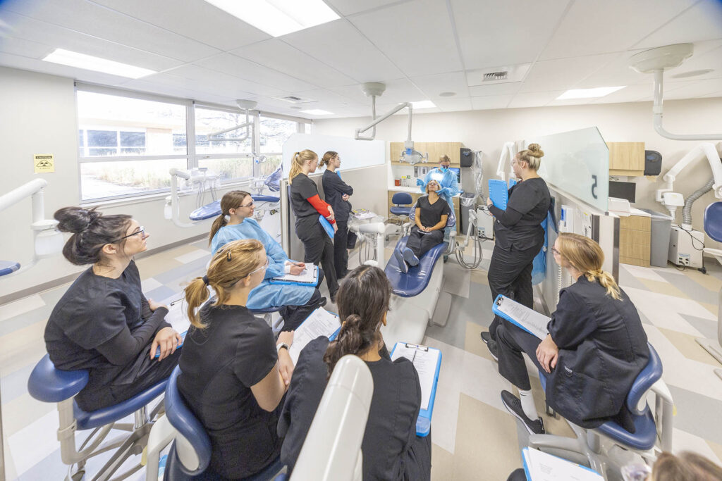 A group of Sheridan College Dental Hygiene students surrounding a dental chair as the instructor demonstrates a technique.