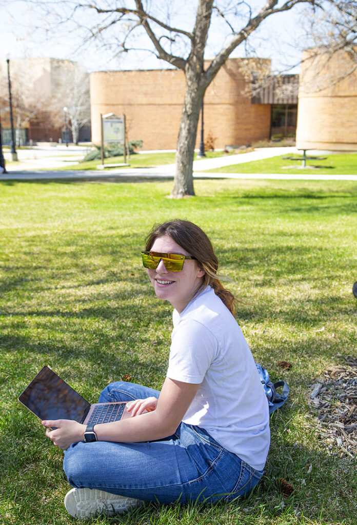 Student with their laptop in the grass at Sheridan College