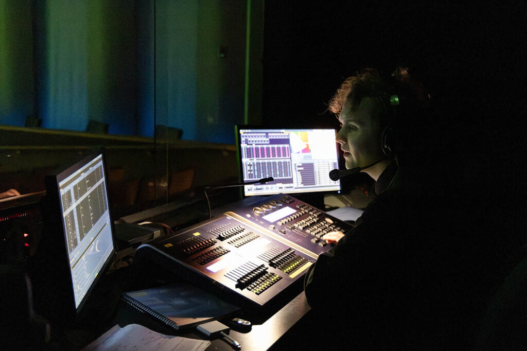 Student working in the dark sound booth in Kinnison Hall with faders and multiple screens